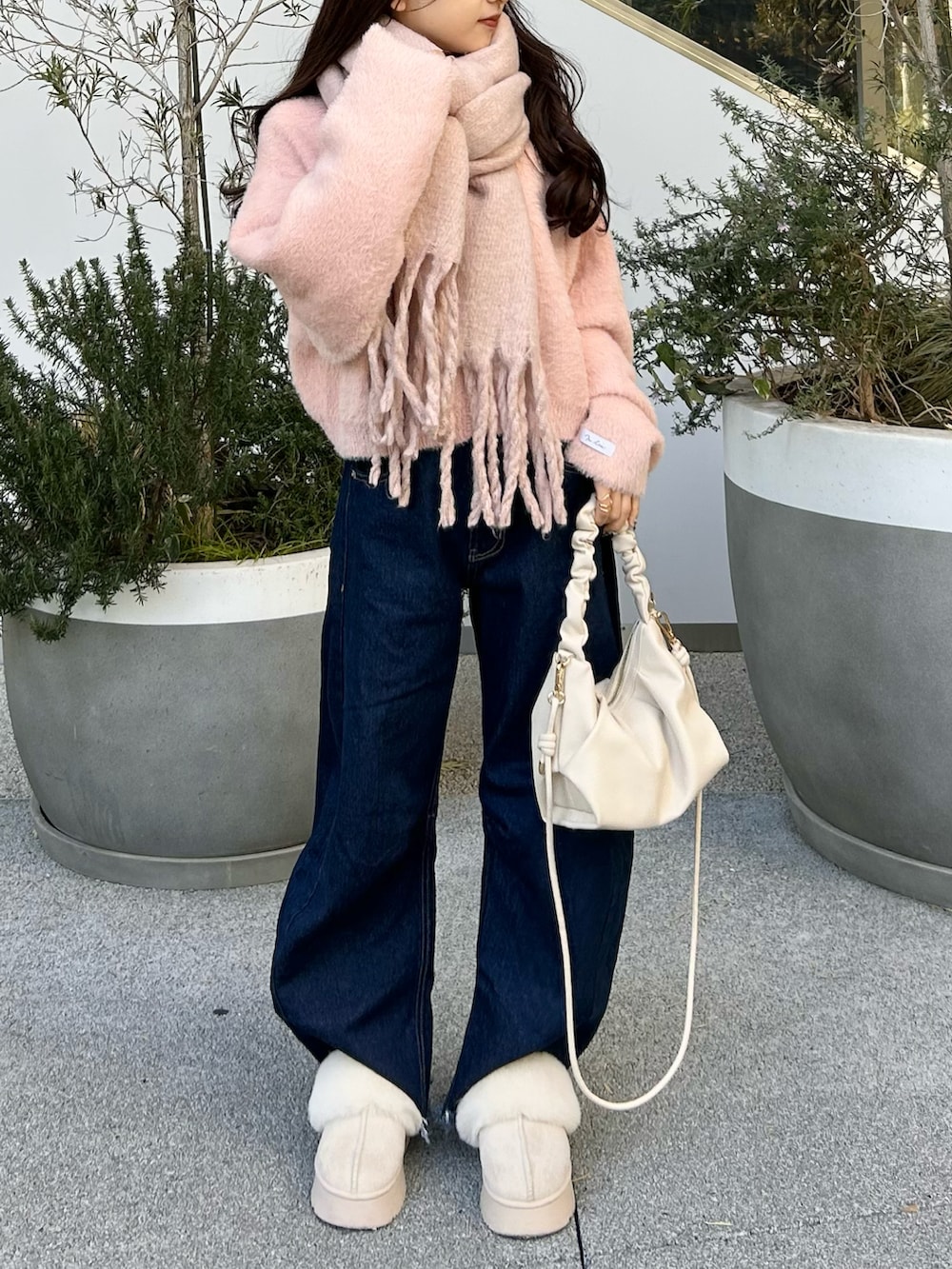 ブルー系のデニムパンツ、ピンク系のニット/セーター、ホワイト系のショルダーバッグを着用したレディースの冬コーディネートの3枚目の写真