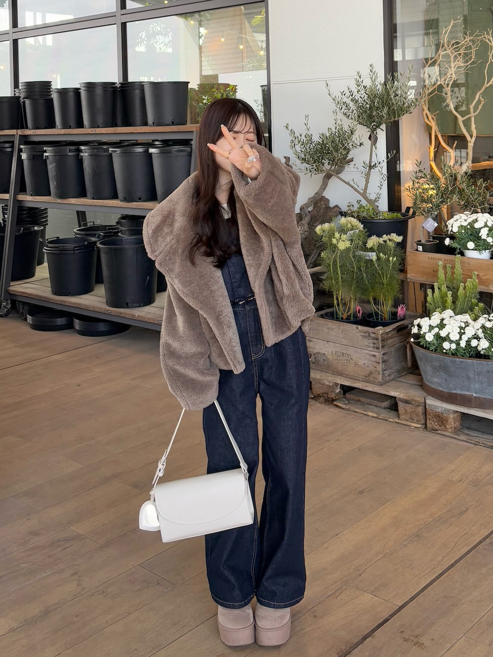 ブルー系のデニムパンツ、ブラウン系のブルゾン、ホワイト系のショルダーバッグを着用したレディースの冬コーディネートの2枚目の写真