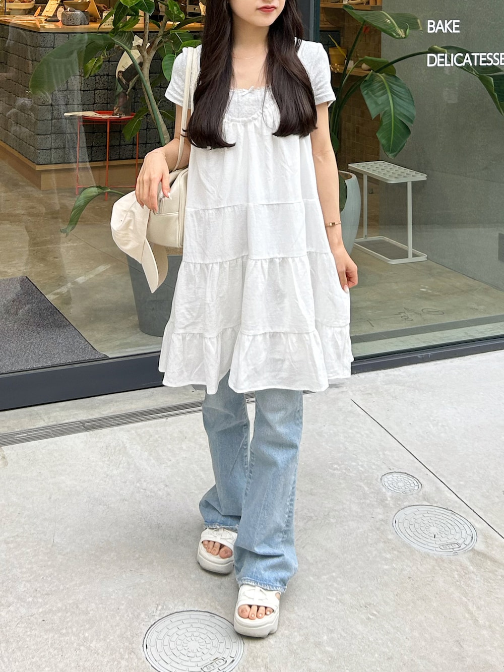 ブルー系のデニムパンツ、ホワイト系のワンピース、ホワイト系のショルダーバッグを着用したレディースの夏コーディネートの3枚目の写真