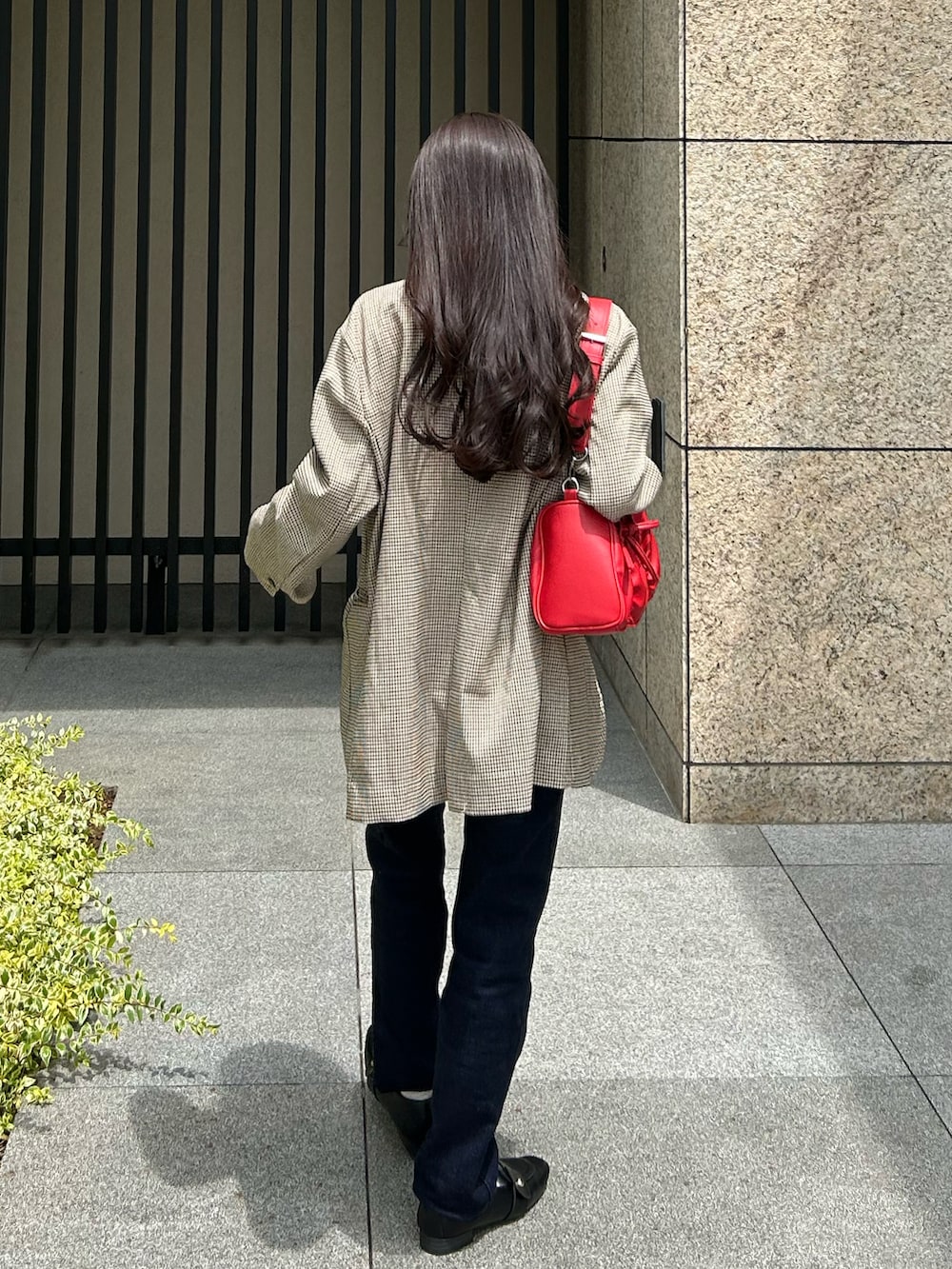 ブルー系のデニムパンツ、ベージュ系のテーラードジャケット、レッド系のショルダーバッグを着用したレディースの夏コーディネートの3枚目の写真