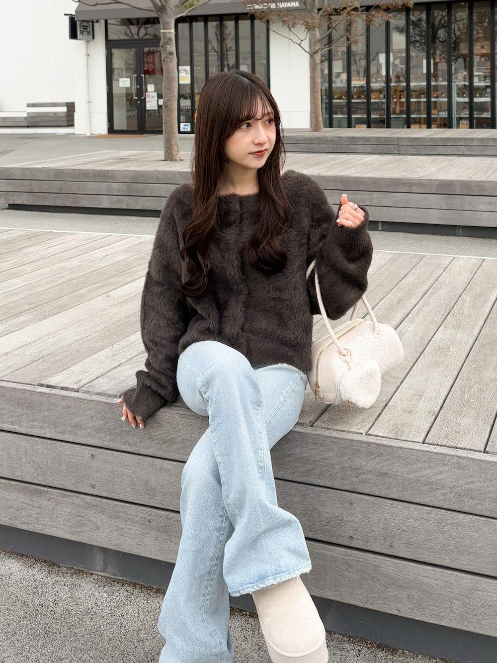 ブラウン系のカーディガン/ボレロ、ブルー系のデニムパンツ、ホワイト系のボストンバッグを着用したレディースの春コーディネートの4枚目の写真