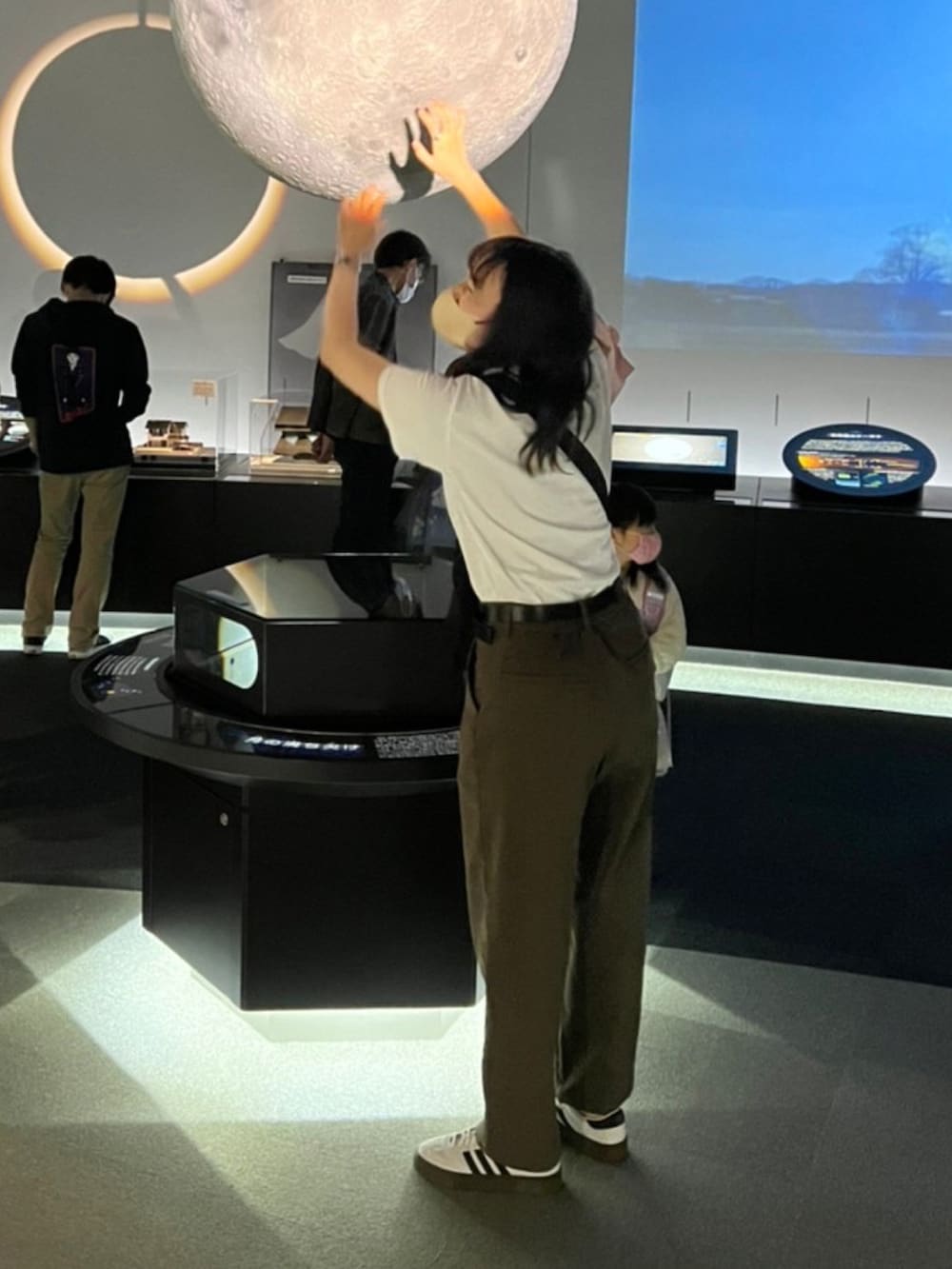 ブラウン系のパンツ、ホワイト系のスニーカー、ブラック系のショルダーバッグを着用したレディースの春コーディネートの2枚目の写真