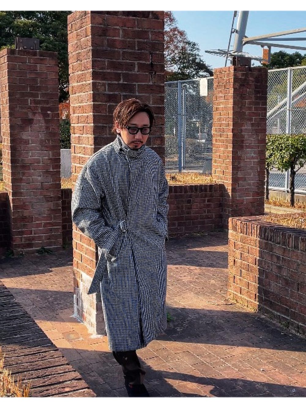 イエロー系のニット/セーター、ブラック系のチェスターコート、グリーン系のスラックスを着用したメンズの冬コーディネートの5枚目の写真