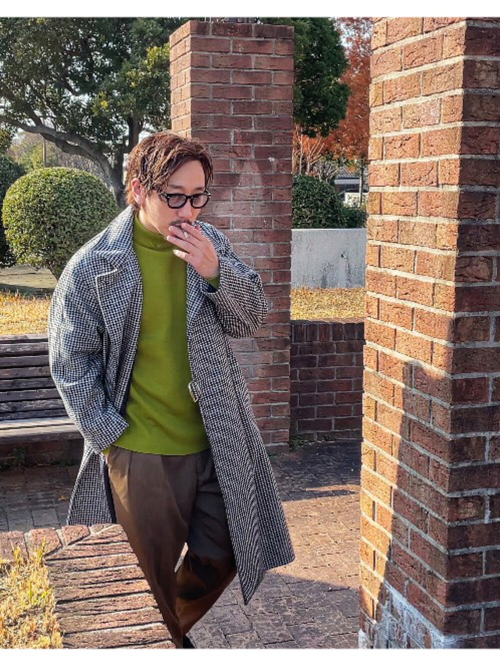 イエロー系のニット/セーター、ブラック系のチェスターコート、グリーン系のスラックスを着用したメンズの冬コーディネートの4枚目の写真