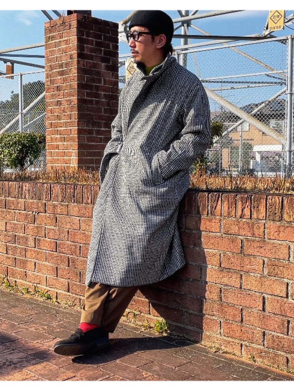 イエロー系のニット/セーター、ブラック系のチェスターコート、グリーン系のスラックスを着用したメンズの冬コーディネートの3枚目の写真