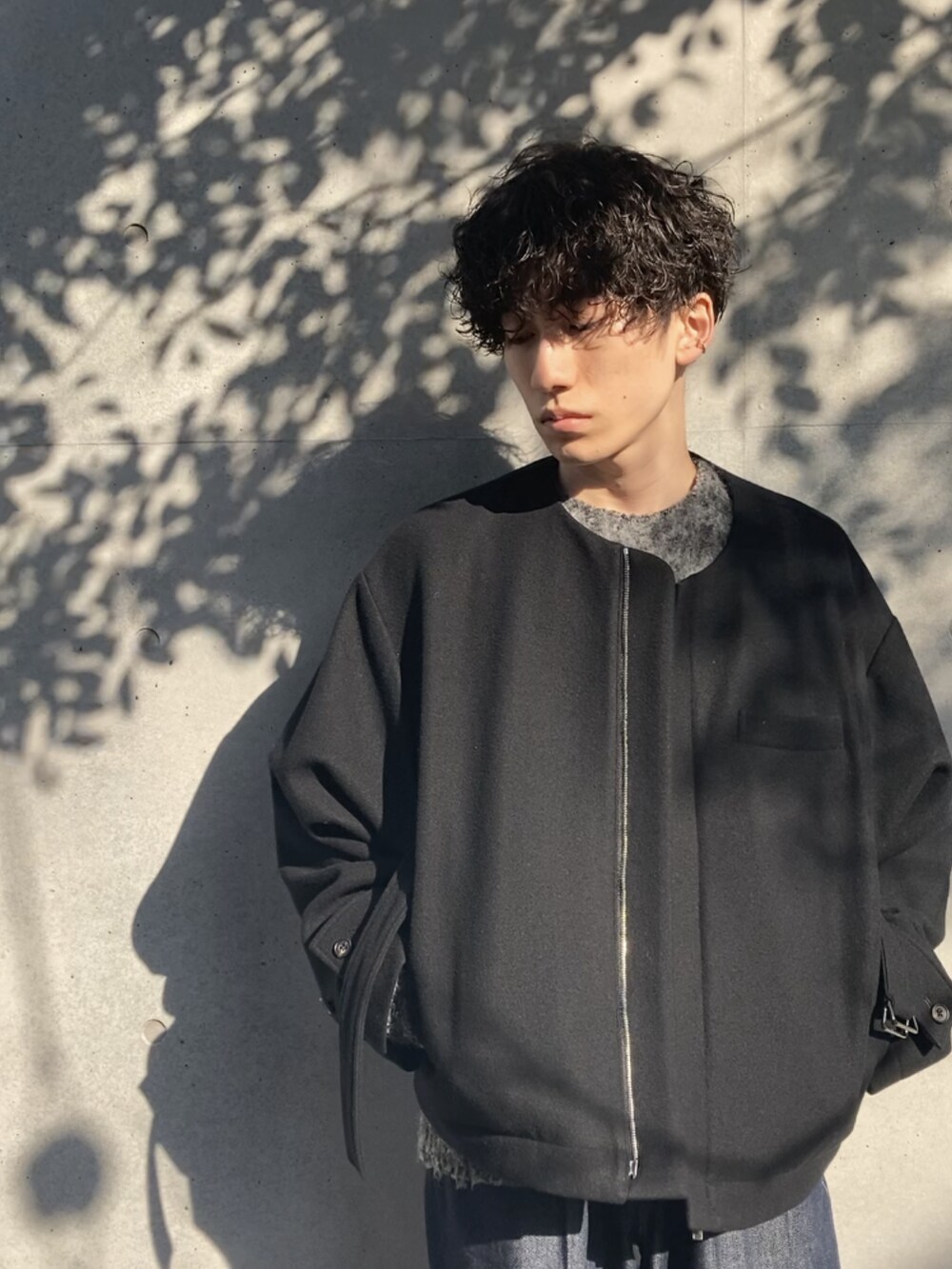 ブラック系のノーカラージャケット、グレー系のニット/セーター、ブルー系のデニムパンツを着用したメンズの冬コーディネートの4枚目の写真