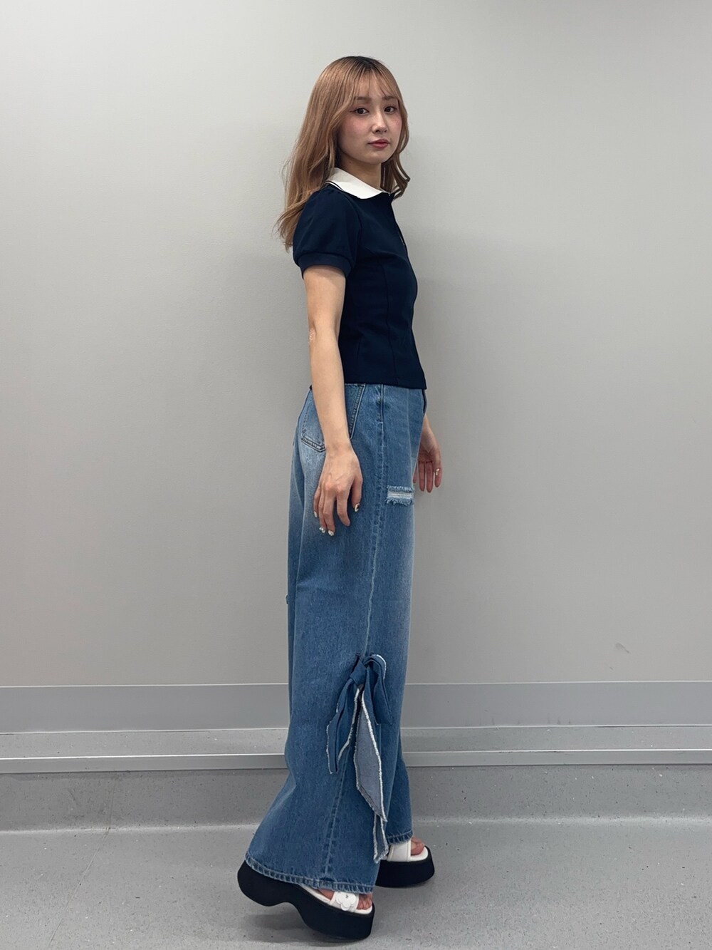 ブルー系のデニムパンツ、ブルー系のポロシャツ、ホワイト系のサンダルを着用したレディースの春コーディネートの2枚目の写真
