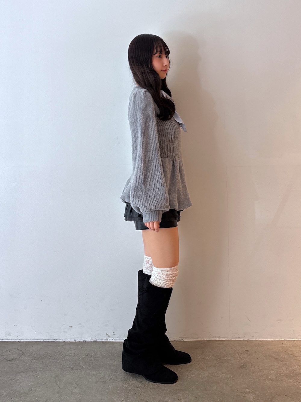 グレー系のニット/セーター、ブラック系のスカート、ブラック系のブーツを着用したレディースの秋コーディネートの2枚目の写真