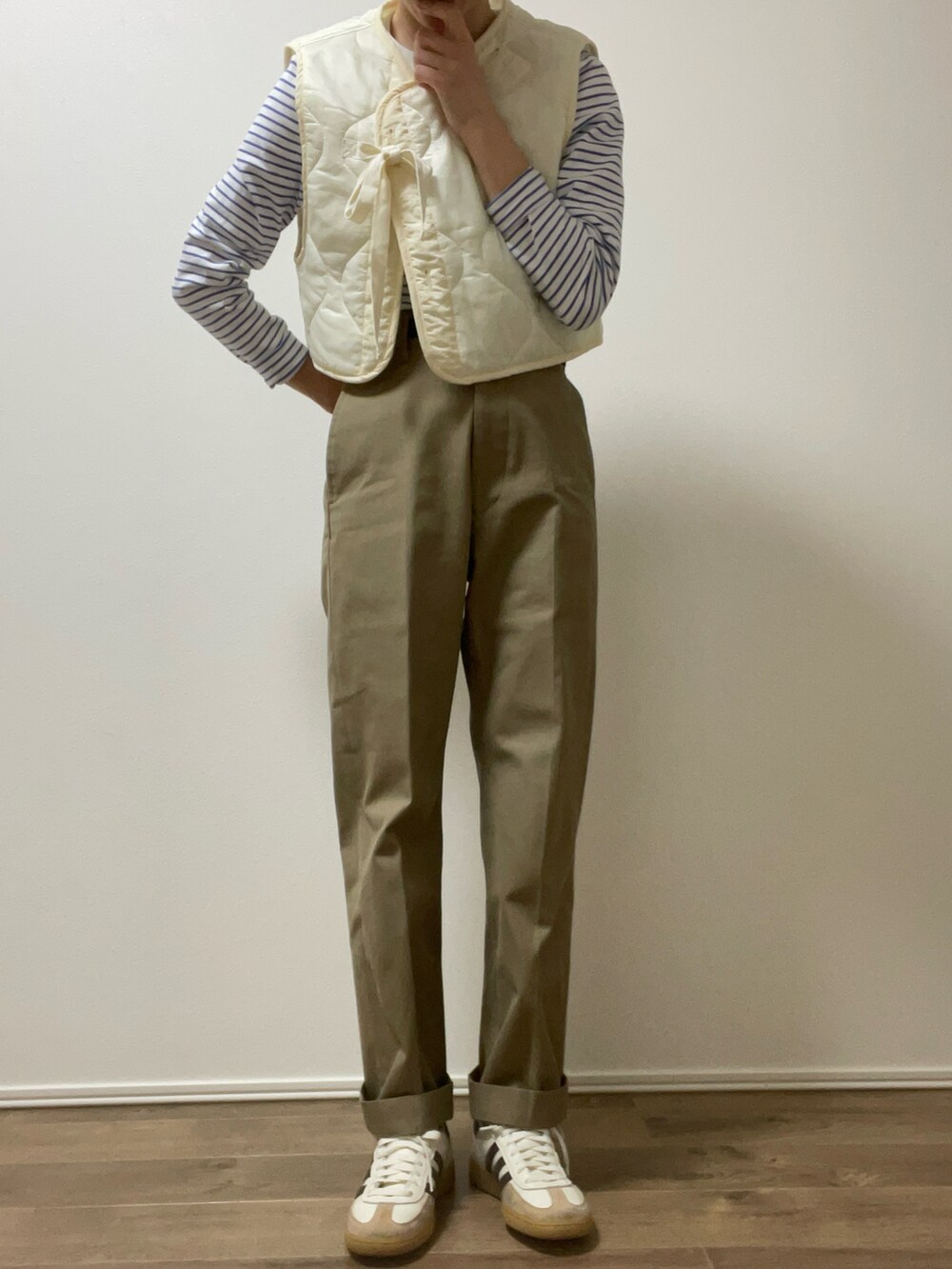 ホワイト系のベスト、ベージュ系のチノパンツ、ホワイト系のスニーカーを着用したレディースの春コーディネートの2枚目の写真