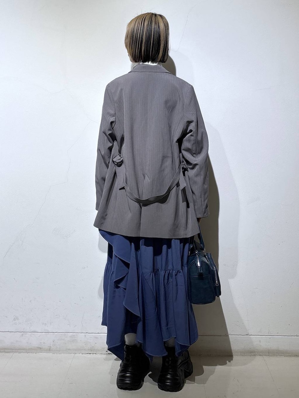 ブラック系のスニーカー、ブルー系のスカート、グレー系のテーラードジャケットを着用したレディースの冬コーディネートの4枚目の写真