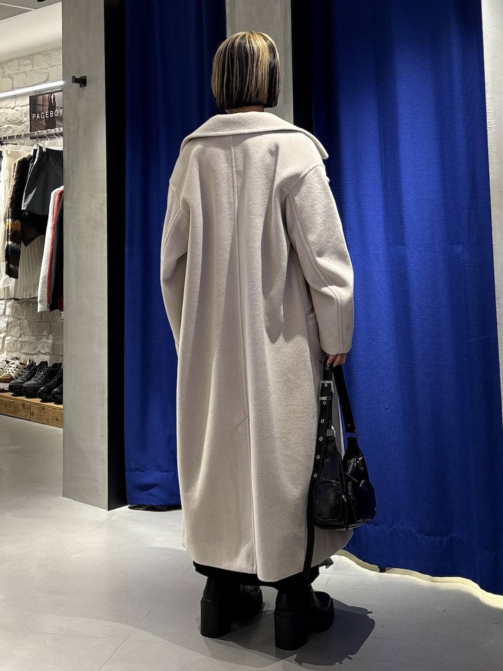 ベージュ系のチェスターコート、グリーン系のニット/セーター、ブラック系のブーツを着用したレディースの冬コーディネートの4枚目の写真