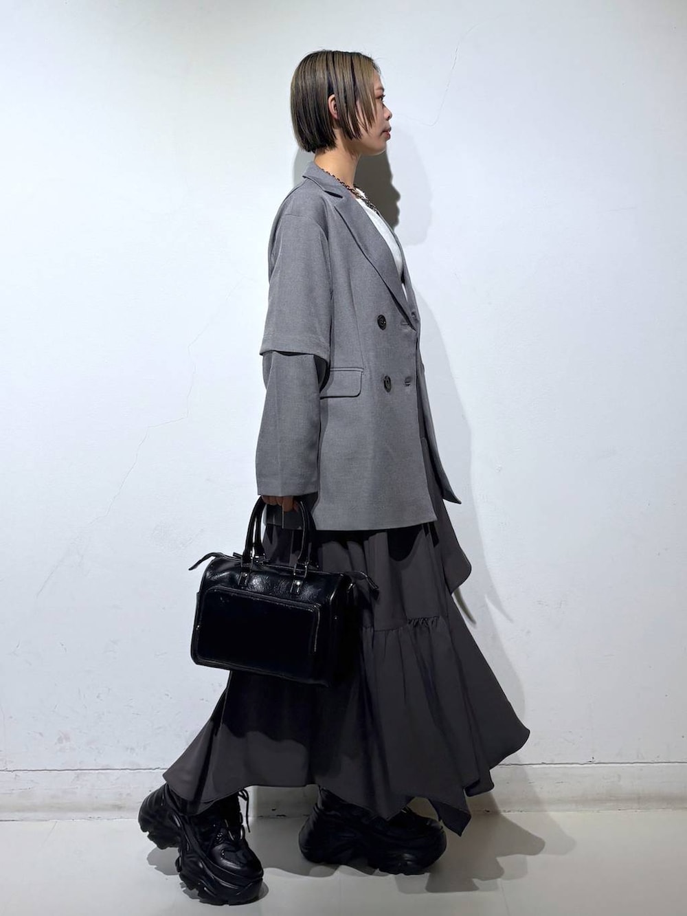 ブラック系のスニーカー、グレー系のスカート、ブラック系のショルダーバッグを着用したレディースの春コーディネートの3枚目の写真