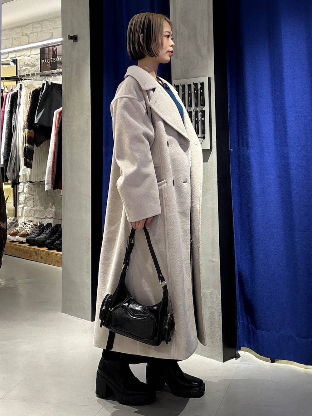 ベージュ系のチェスターコート、グリーン系のニット/セーター、ブラック系のブーツを着用したレディースの冬コーディネートの3枚目の写真