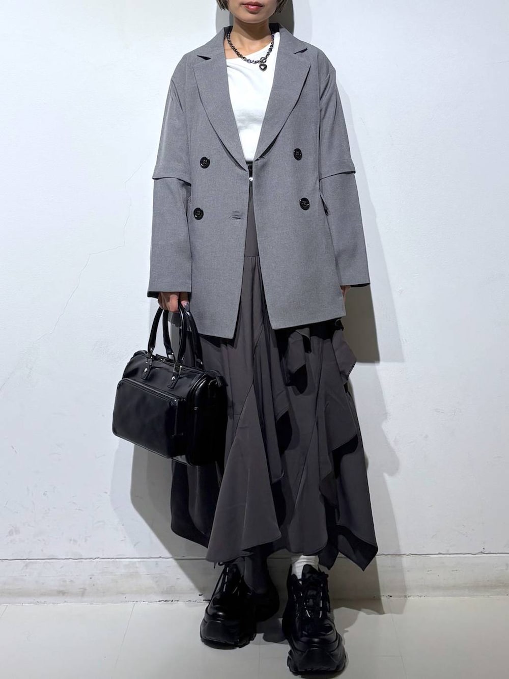 ブラック系のスニーカー、グレー系のスカート、ブラック系のショルダーバッグを着用したレディースの春コーディネートの2枚目の写真