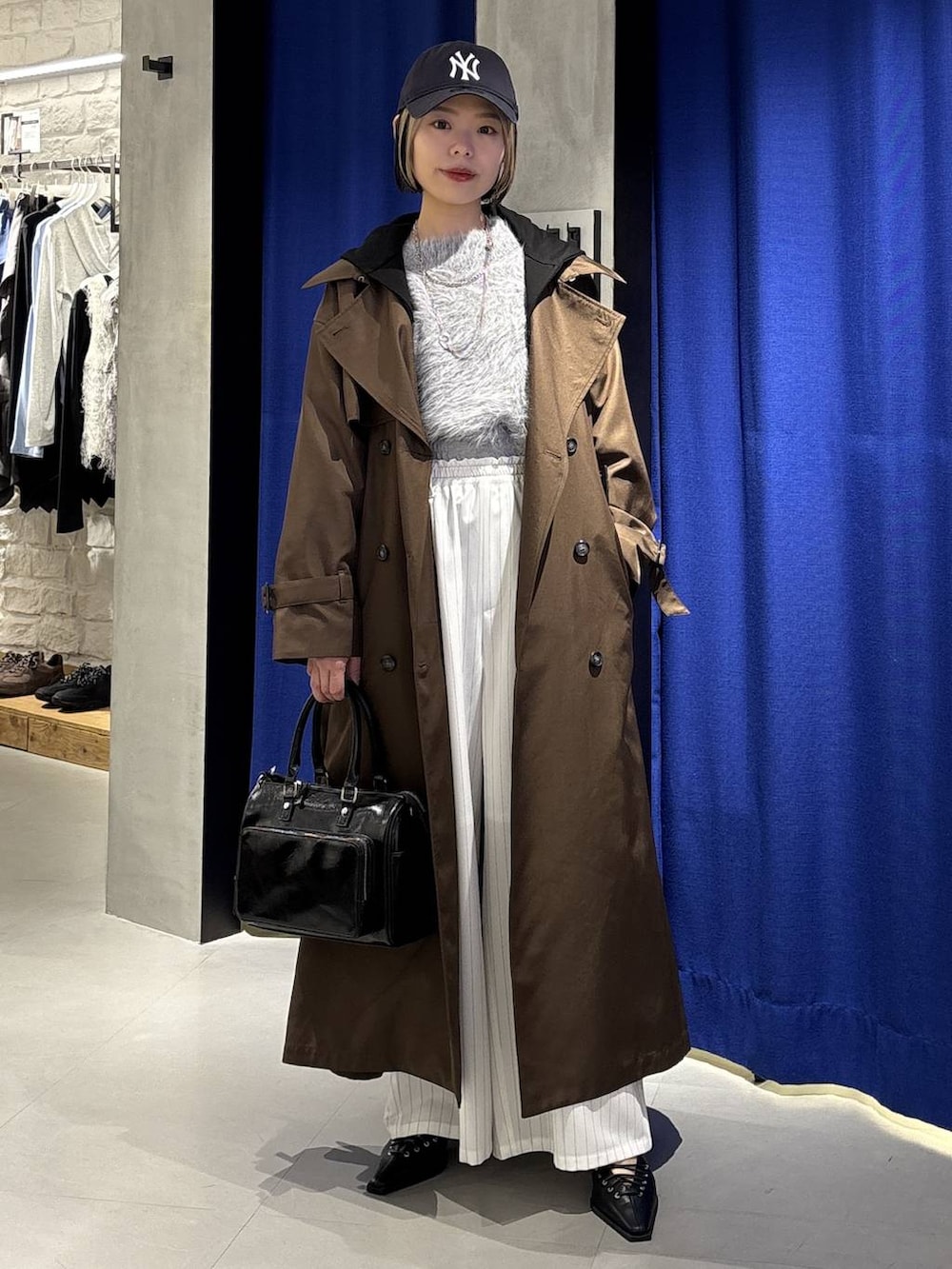 グレー系のニット/セーター、ブラウン系のトレンチコート、ブラック系のショルダーバッグを着用したレディースの冬コーディネートの3枚目の写真