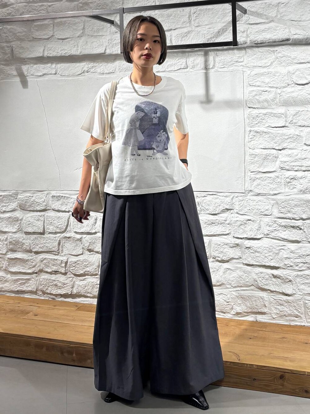 グレー系のスラックス、ホワイト系のTシャツ/カットソー、ホワイト系のショルダーバッグを着用したレディースの夏コーディネートの2枚目の写真