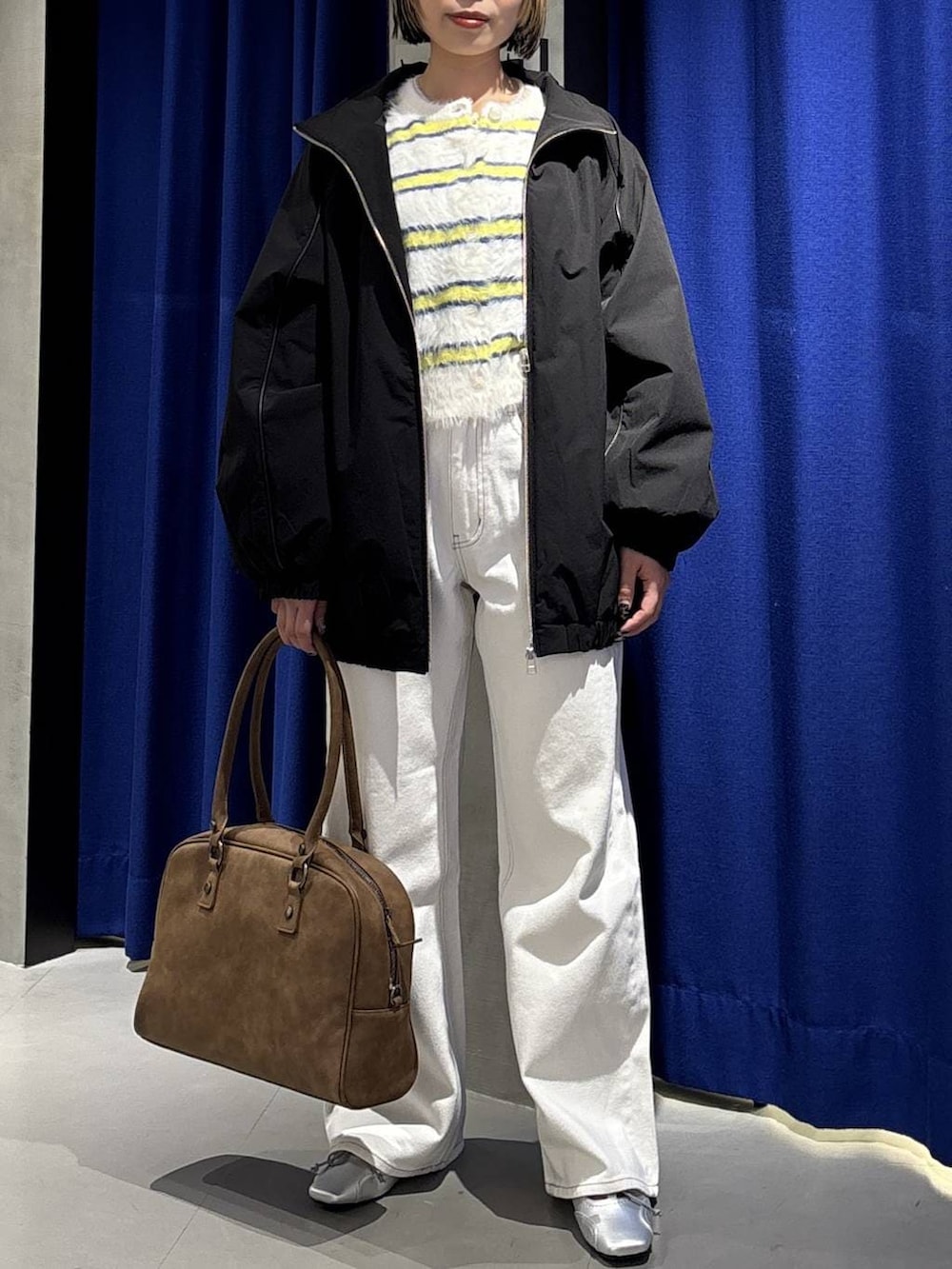 ベージュ系のボストンバッグ、ホワイト系のスラックス、ブラック系のナイロンジャケットを着用したレディースの冬コーディネートの2枚目の写真