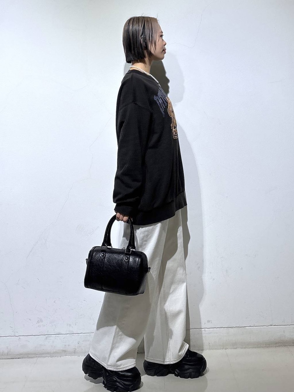 ブラック系のブーツ、ホワイト系のスラックス、ブラック系のボストンバッグを着用したレディースの冬コーディネートの3枚目の写真