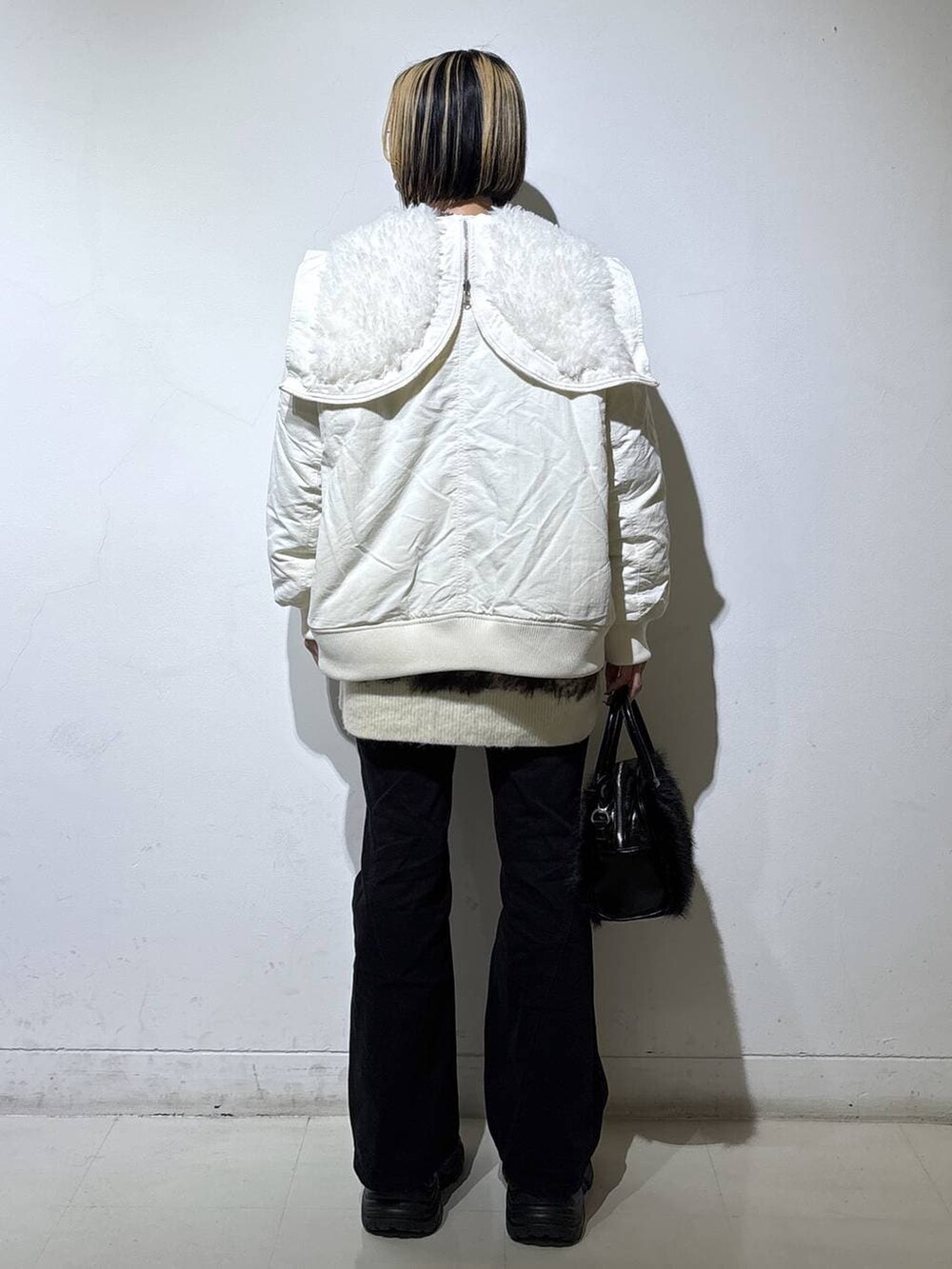 ブラック系のスニーカー、ブラック系のデニムパンツ、ホワイト系のブルゾンを着用したレディースの冬コーディネートの4枚目の写真