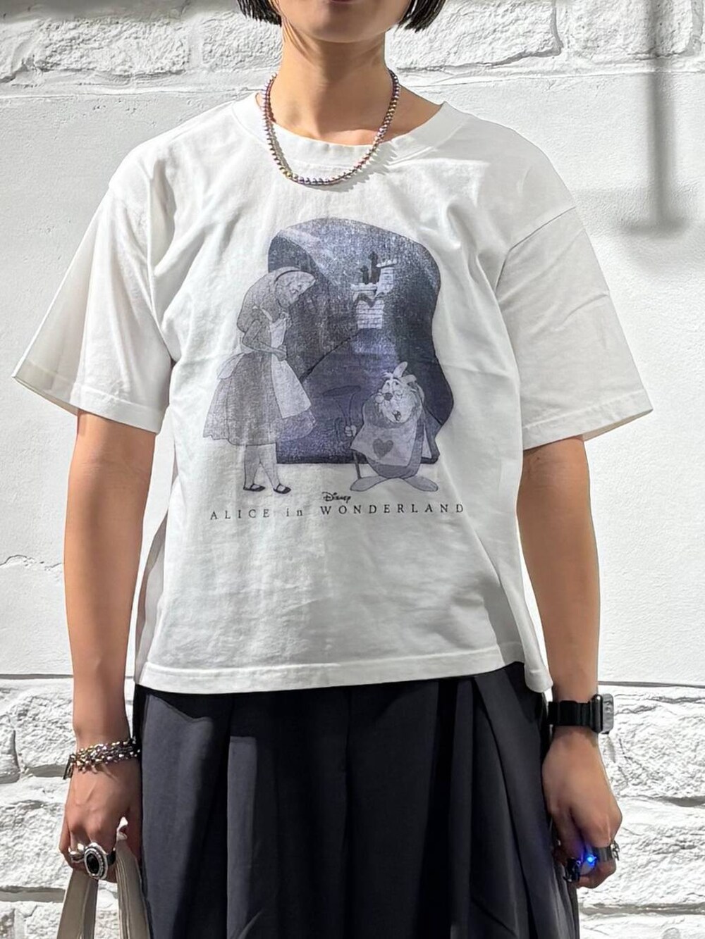 グレー系のスラックス、ホワイト系のTシャツ/カットソー、ホワイト系のショルダーバッグを着用したレディースの夏コーディネートの4枚目の写真