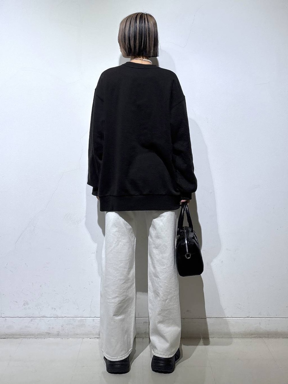 ブラック系のブーツ、ホワイト系のスラックス、ブラック系のボストンバッグを着用したレディースの冬コーディネートの4枚目の写真