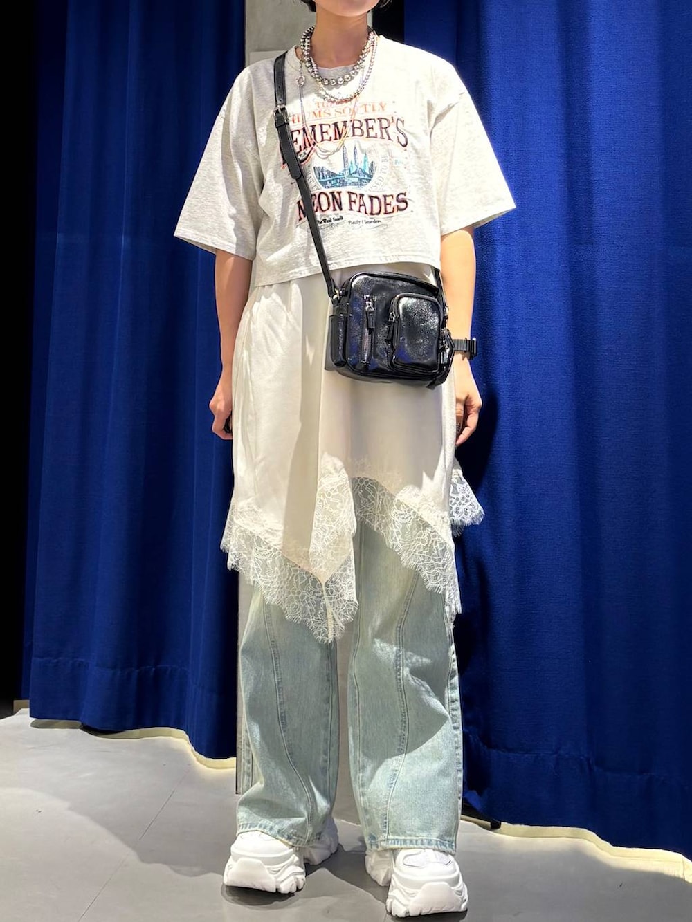 ブラック系のスニーカー、ブルー系のデニムパンツ、ホワイト系のチュニックを着用したレディースの春コーディネートの2枚目の写真