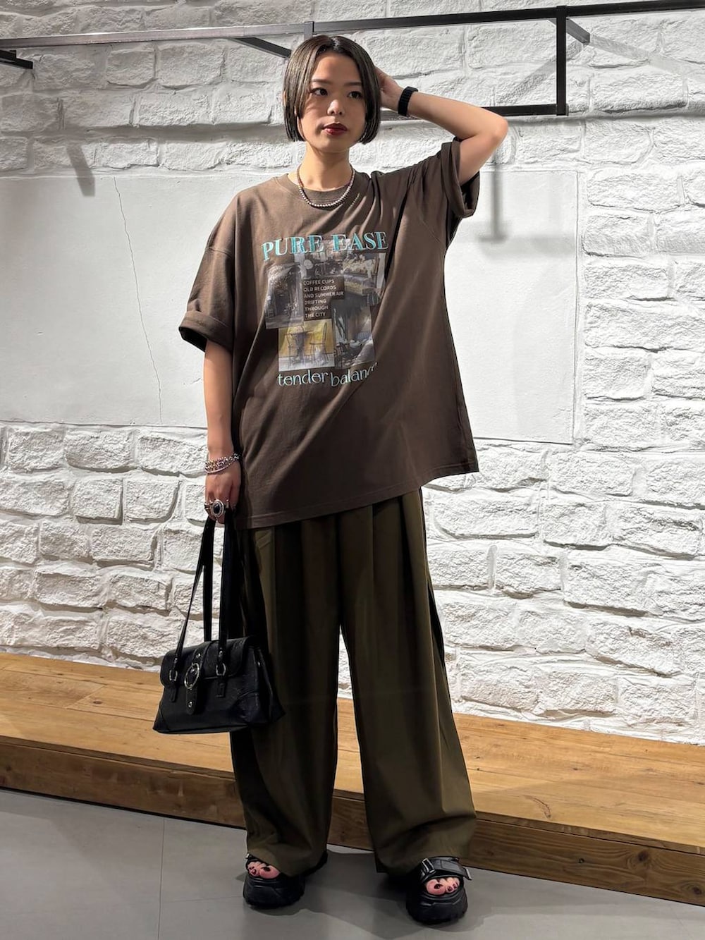グリーン系のスラックス、ブラウン系のTシャツ/カットソー、ブラック系のサンダルを着用したレディースの夏コーディネートの2枚目の写真