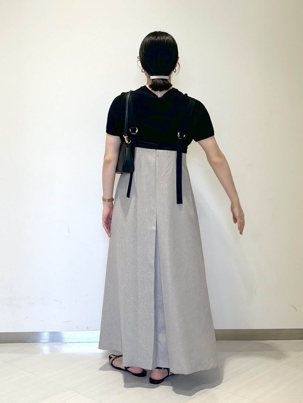 ブラック系のニット/セーター、ブラック系のショルダーバッグ、グレー系のジャンパースカートを着用したレディースの夏コーディネートの4枚目の写真