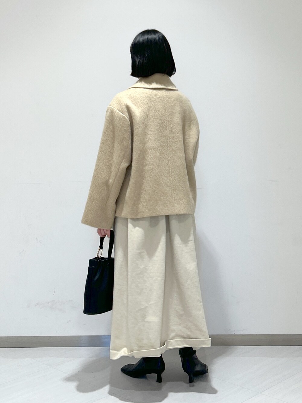 ベージュ系のピーコート、ホワイト系のワンピース、ブラック系のショルダーバッグを着用したレディースの冬コーディネートの3枚目の写真