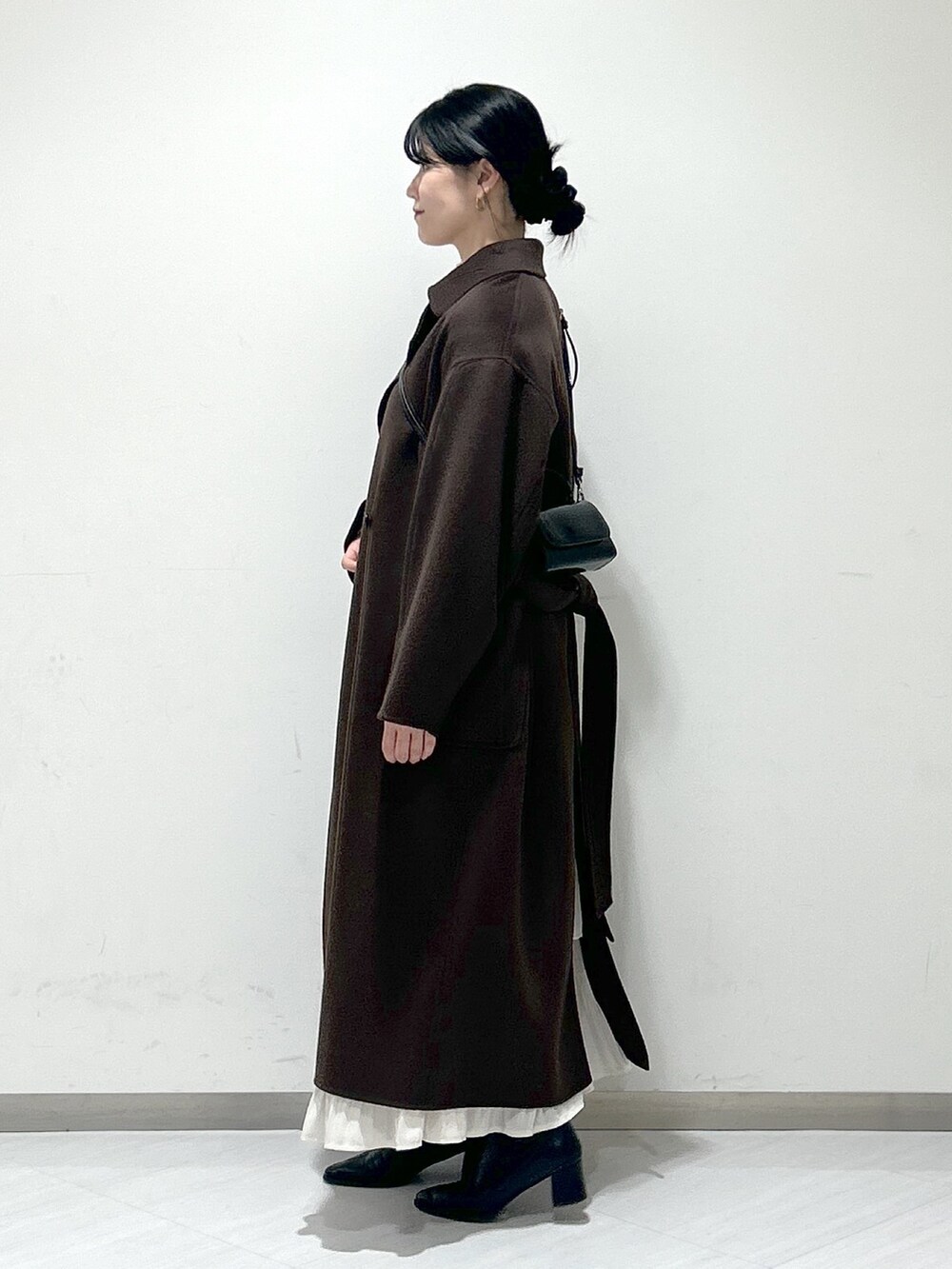 ブラック系のショルダーバッグ、ブラウン系のステンカラーコート、ホワイト系のスカートを着用したレディースの冬コーディネートの2枚目の写真