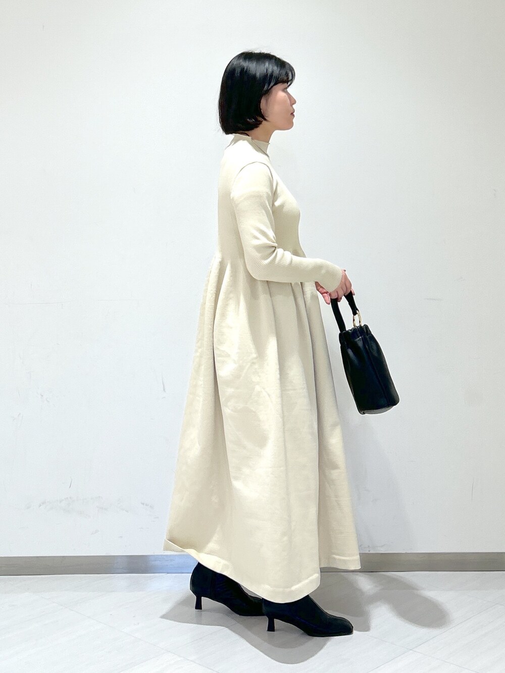 ベージュ系のピーコート、ホワイト系のワンピース、ブラック系のショルダーバッグを着用したレディースの冬コーディネートの7枚目の写真