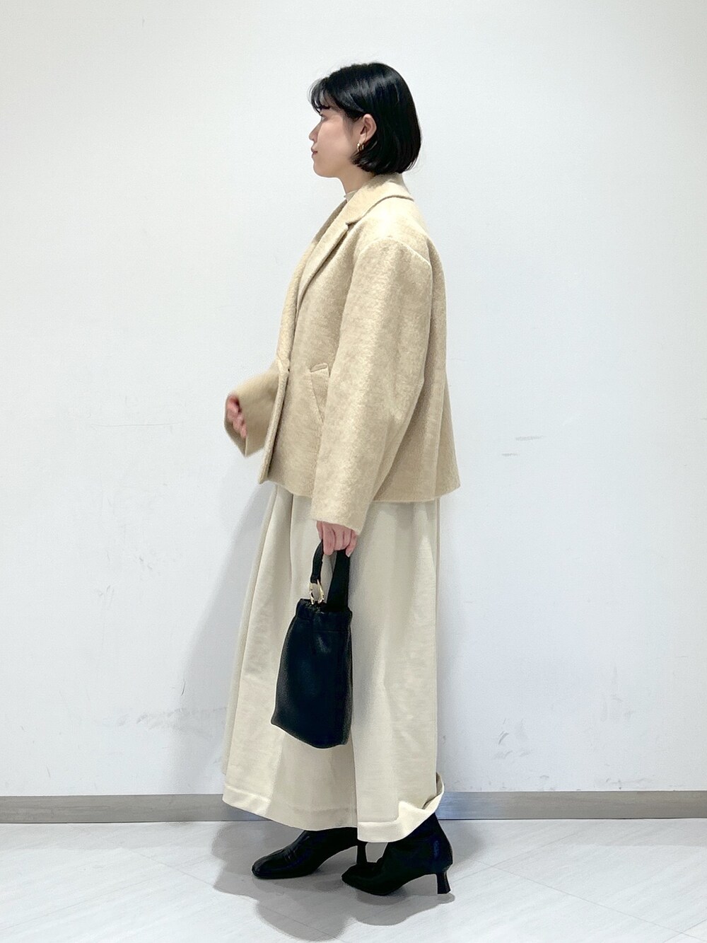 ベージュ系のピーコート、ホワイト系のワンピース、ブラック系のショルダーバッグを着用したレディースの冬コーディネートの2枚目の写真