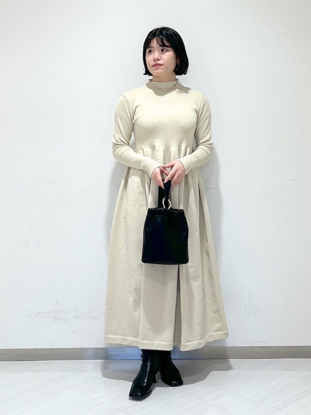 ベージュ系のピーコート、ホワイト系のワンピース、ブラック系のショルダーバッグを着用したレディースの冬コーディネートの5枚目の写真