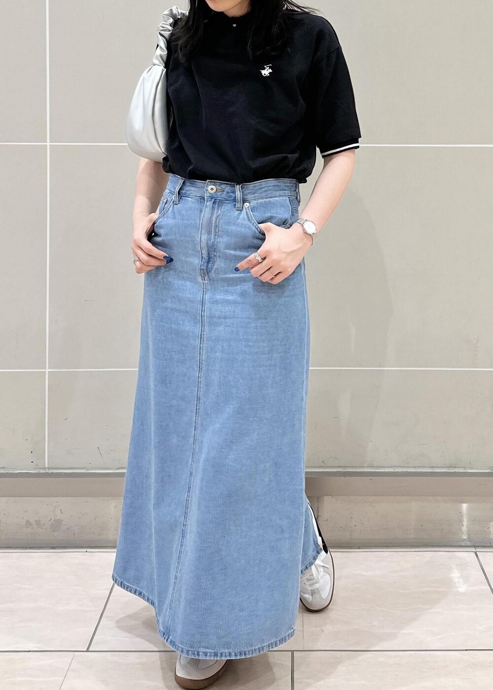 ブルー系のデニムスカート、シルバー系のハンドバッグ、ブラック系のポロシャツを着用したレディースの夏コーディネートの5枚目の写真