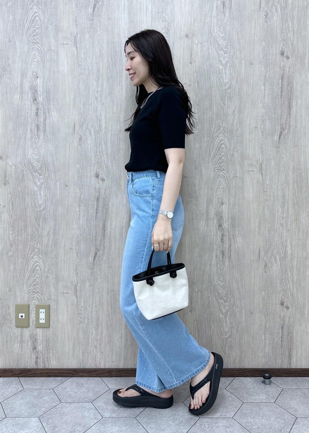 ブルー系のデニムパンツ、ブラック系のニット/セーター、ブラック系のトートバッグを着用したレディースの夏コーディネートの5枚目の写真