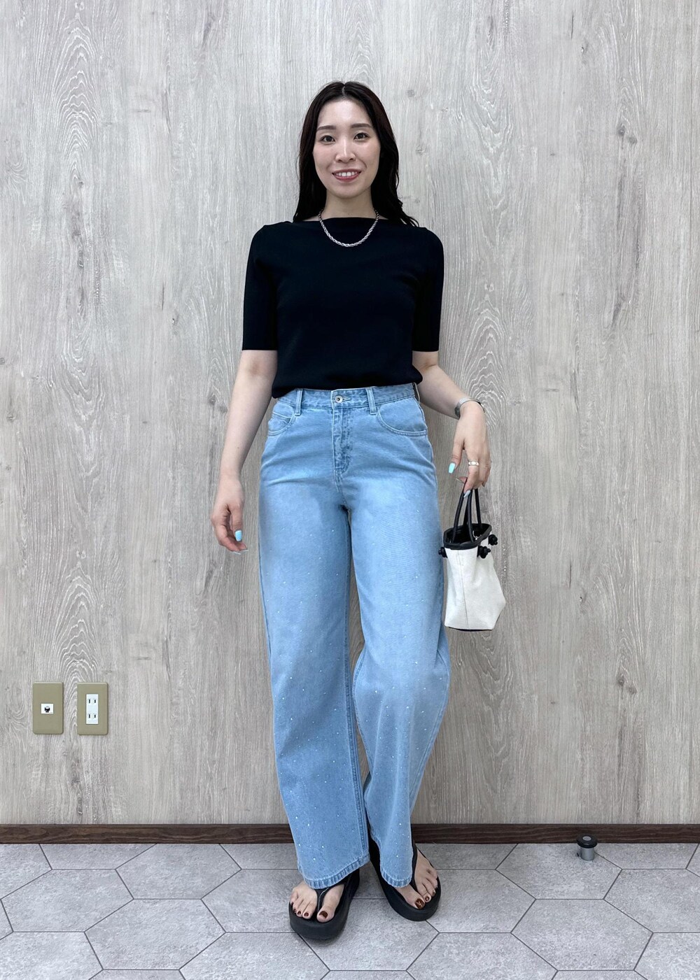 ブルー系のデニムパンツ、ブラック系のニット/セーター、ブラック系のトートバッグを着用したレディースの夏コーディネートの2枚目の写真