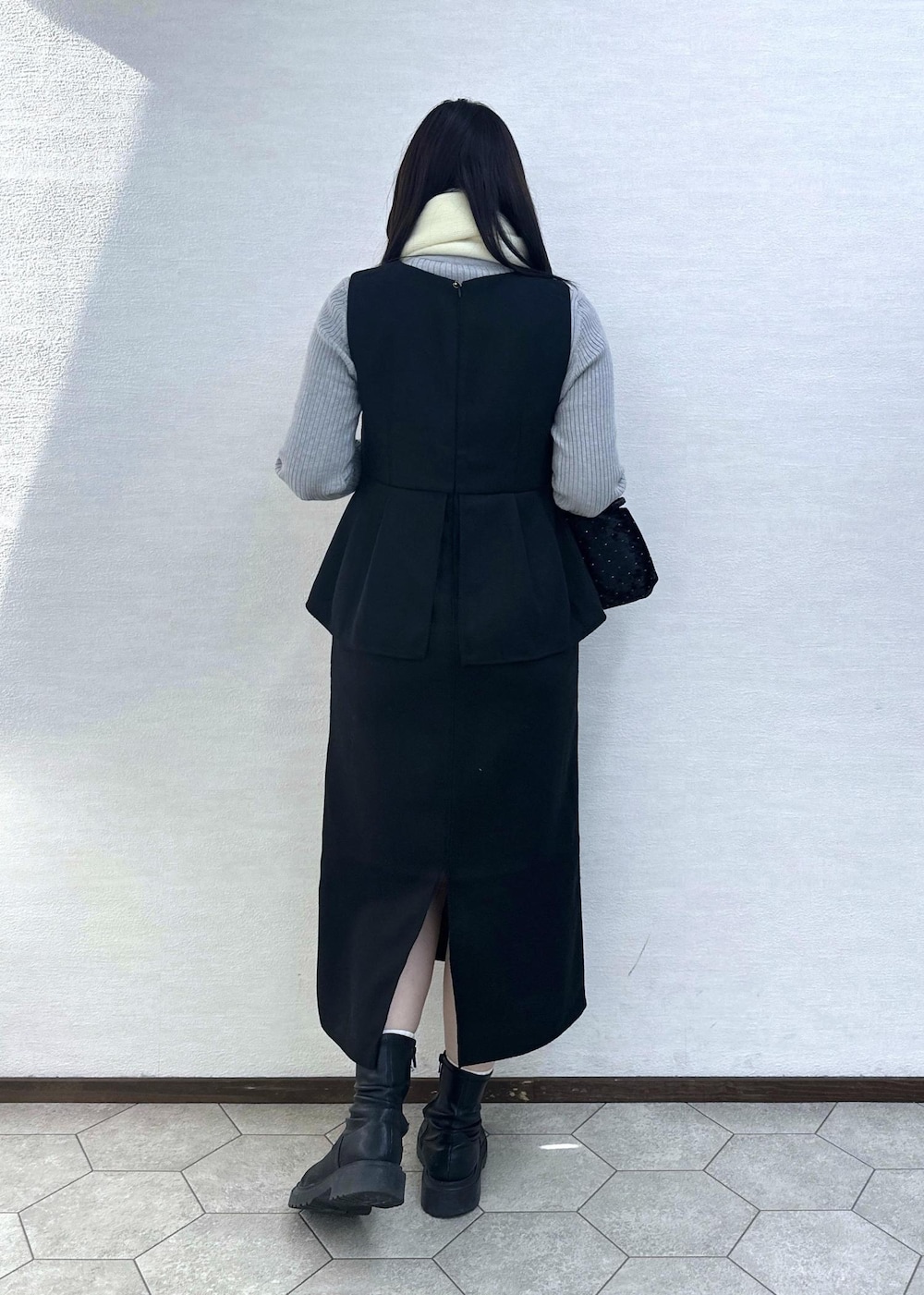 グレー系のニット/セーター、ブラック系のハンドバッグ、ブラック系のジャンパースカートを着用したレディースの冬コーディネートの6枚目の写真