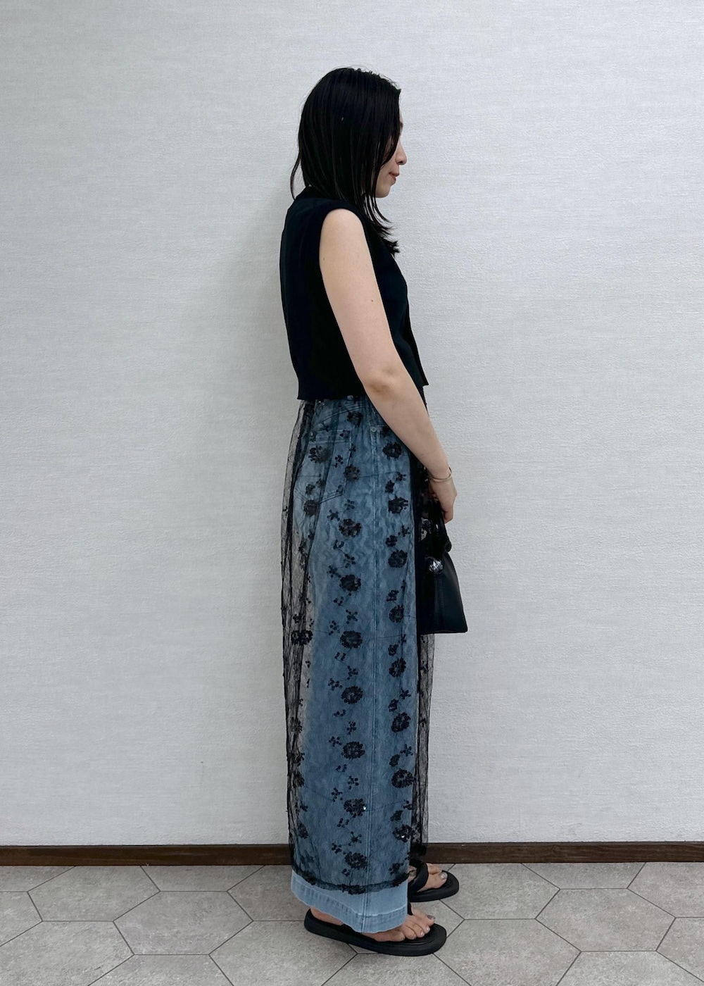 ブルー系のデニムパンツ、ブラック系のベスト、ブラック系のショルダーバッグを着用したレディースの夏コーディネートの6枚目の写真