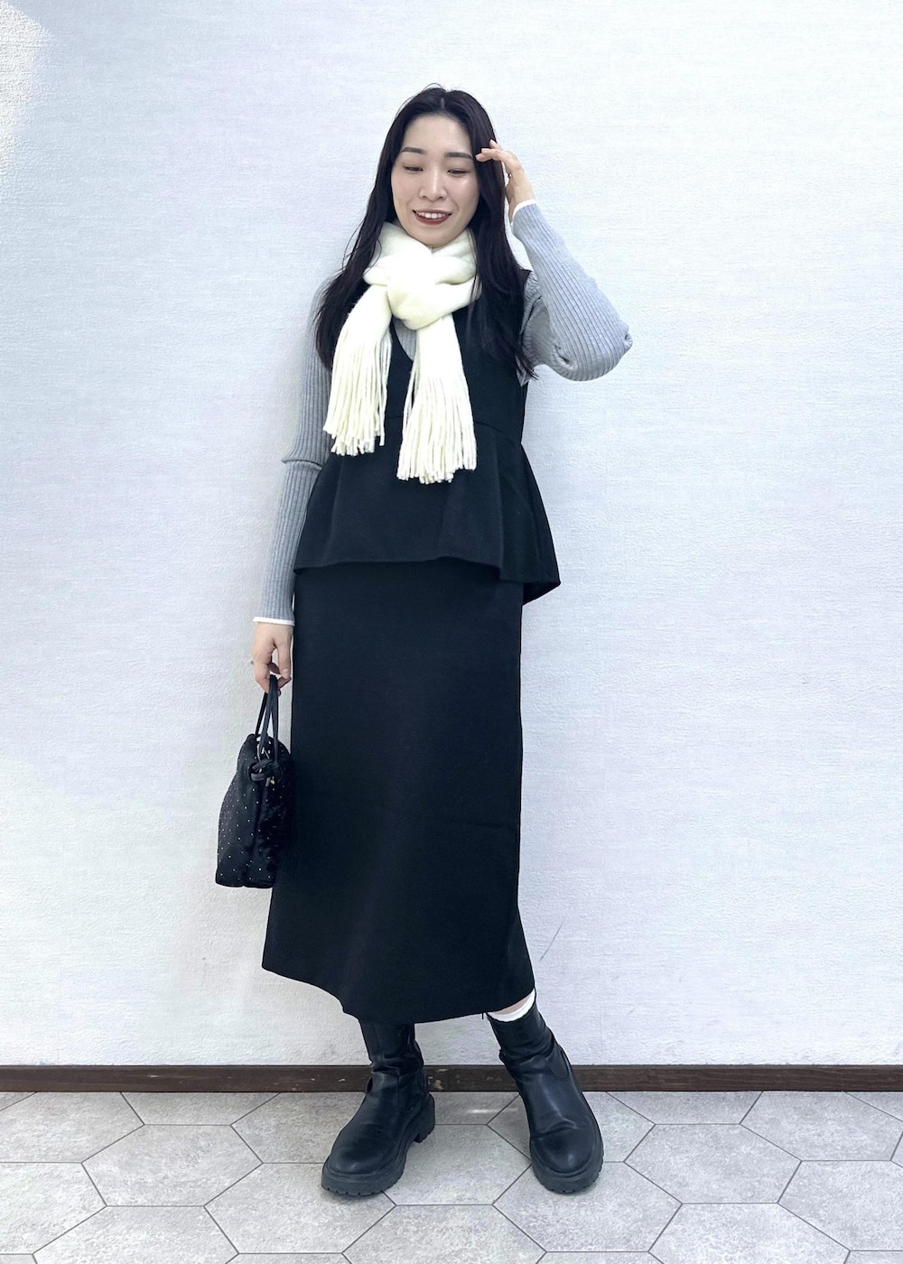 グレー系のニット/セーター、ブラック系のハンドバッグ、ブラック系のジャンパースカートを着用したレディースの冬コーディネートの3枚目の写真