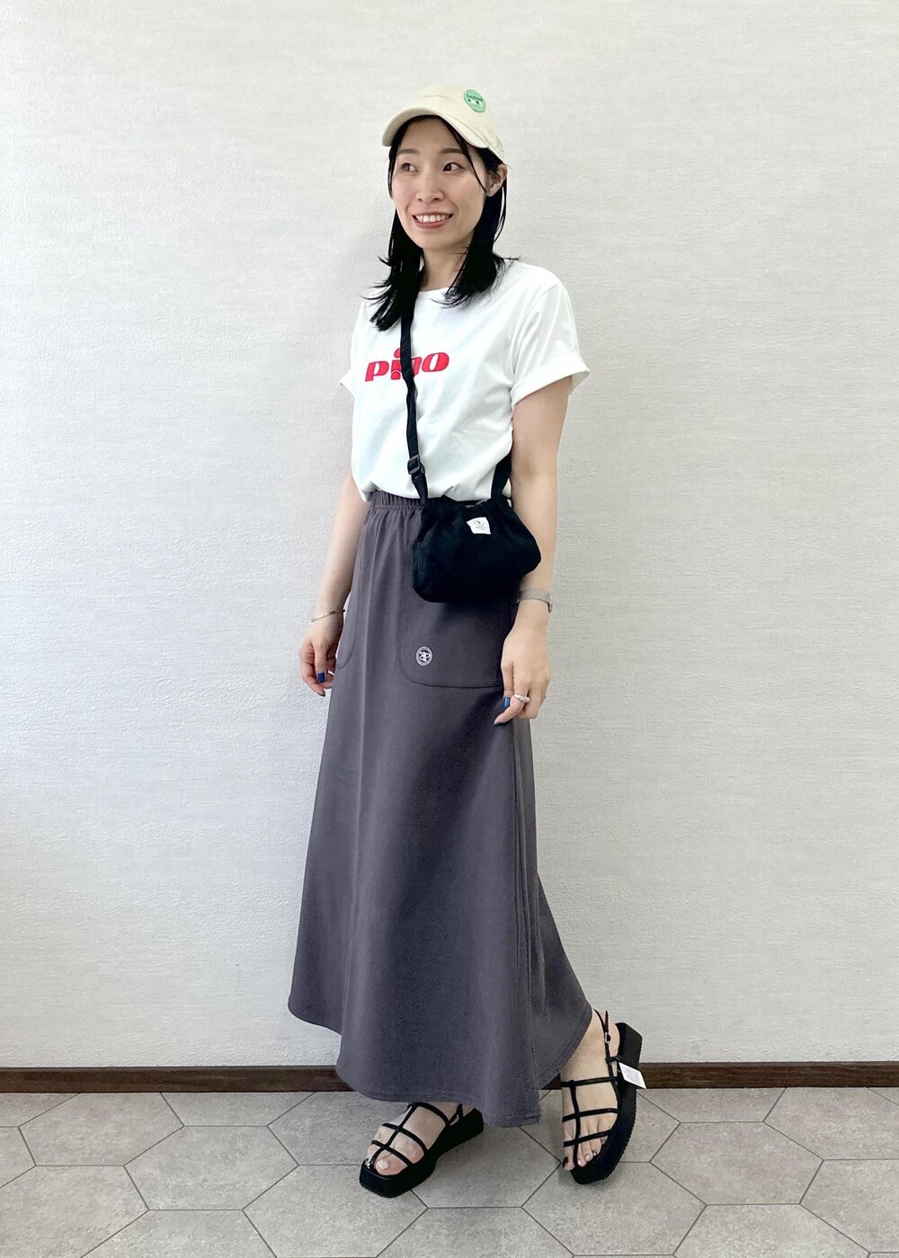 ブラック系のショルダーバッグ、グレー系のスカート、ブラック系のサンダルを着用したレディースの春コーディネートの2枚目の写真