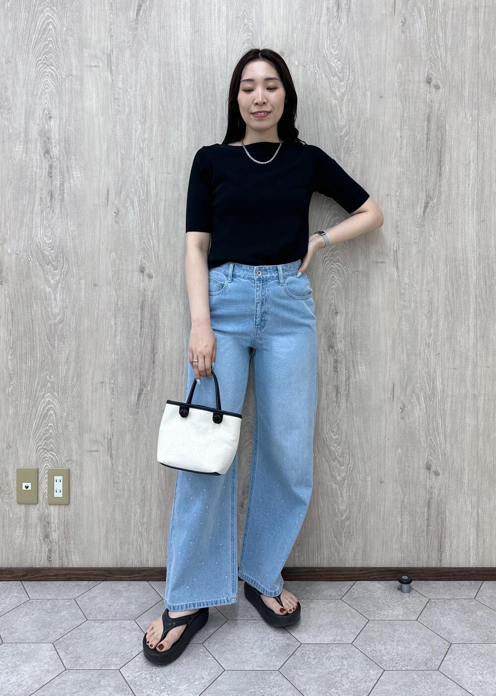 ブルー系のデニムパンツ、ブラック系のニット/セーター、ブラック系のトートバッグを着用したレディースの夏コーディネートの3枚目の写真