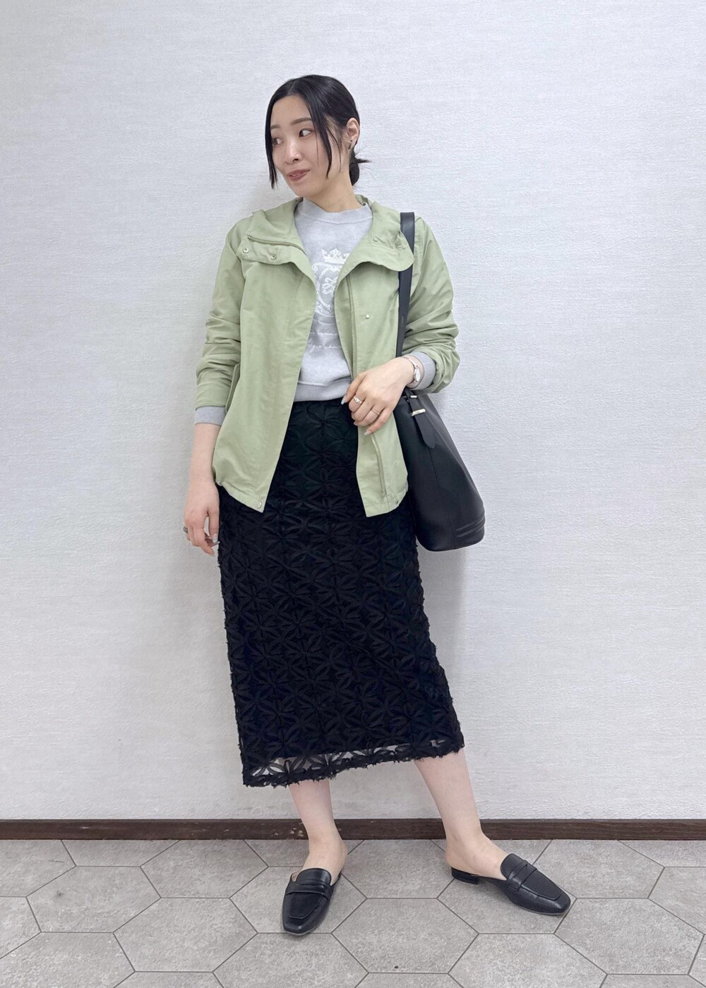 ブラック系のスカート、グレー系のニット/セーター、グリーン系のマウンテンパーカーを着用したレディースの春コーディネートの2枚目の写真