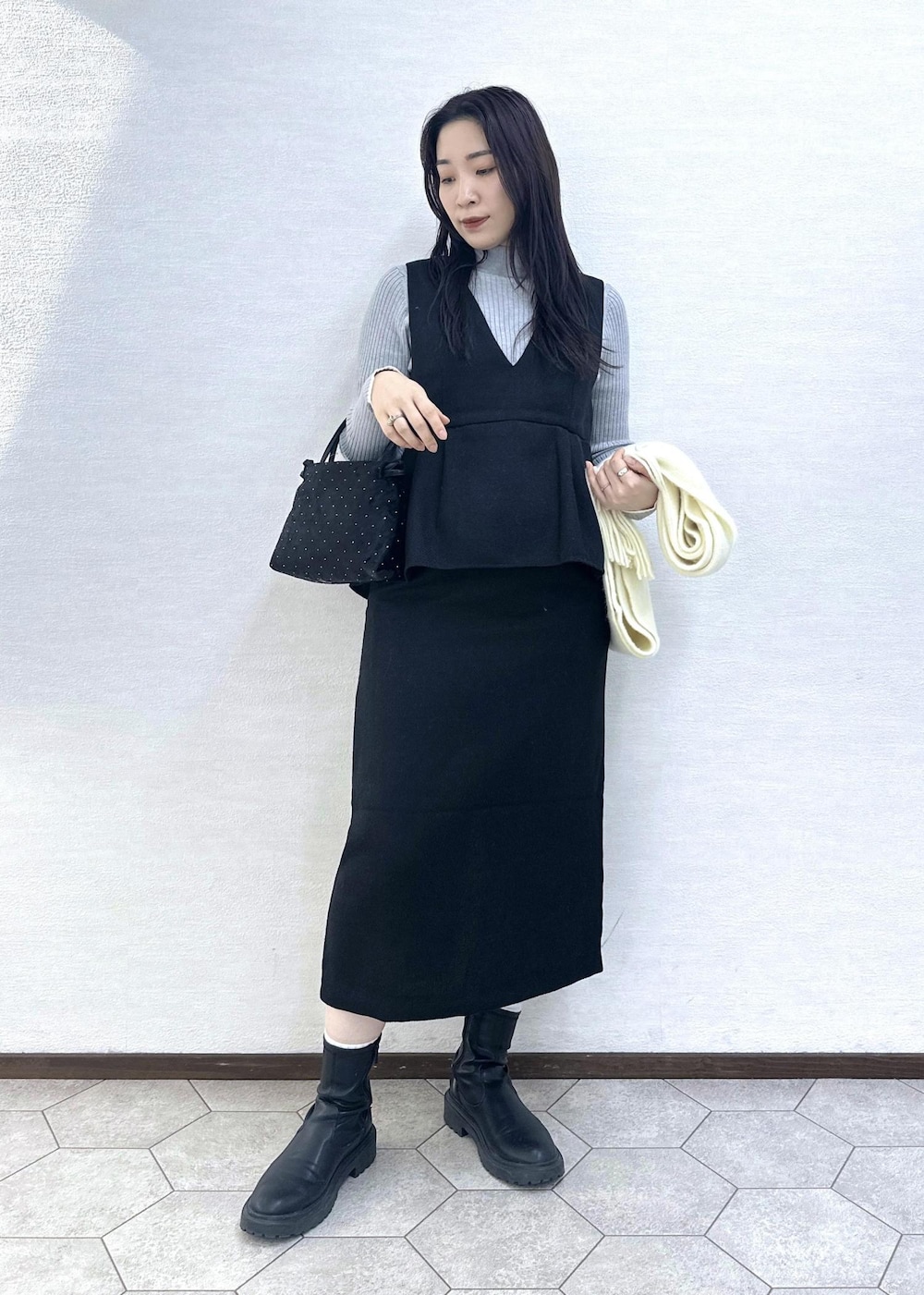 グレー系のニット/セーター、ブラック系のハンドバッグ、ブラック系のジャンパースカートを着用したレディースの冬コーディネートの8枚目の写真