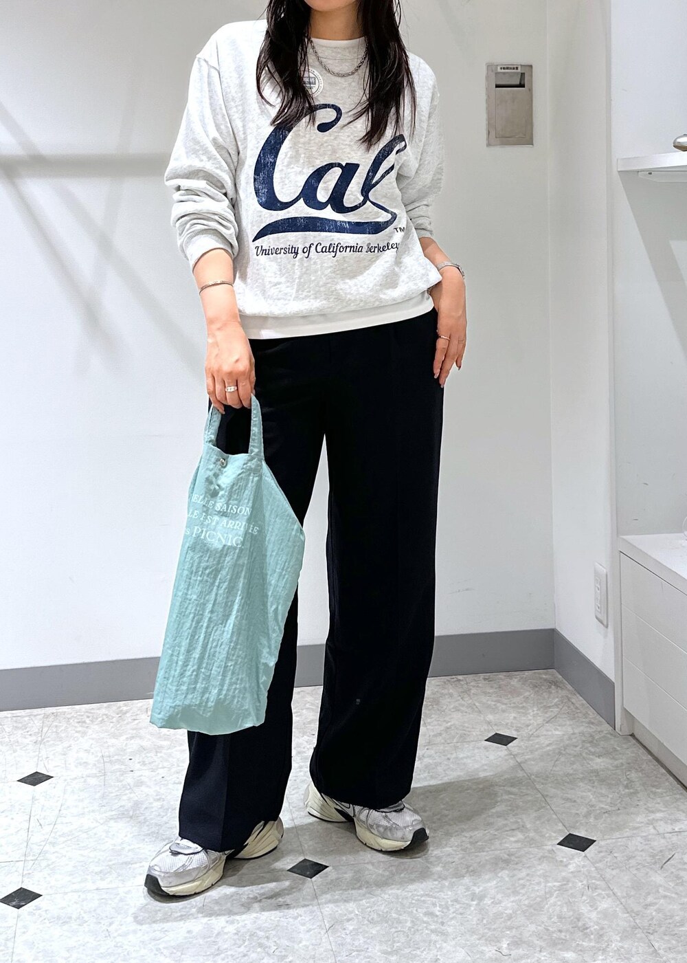 グレー系のスウェット、ブルー系のトートバッグ、ブルー系のスラックスを着用したレディースの夏コーディネートの4枚目の写真