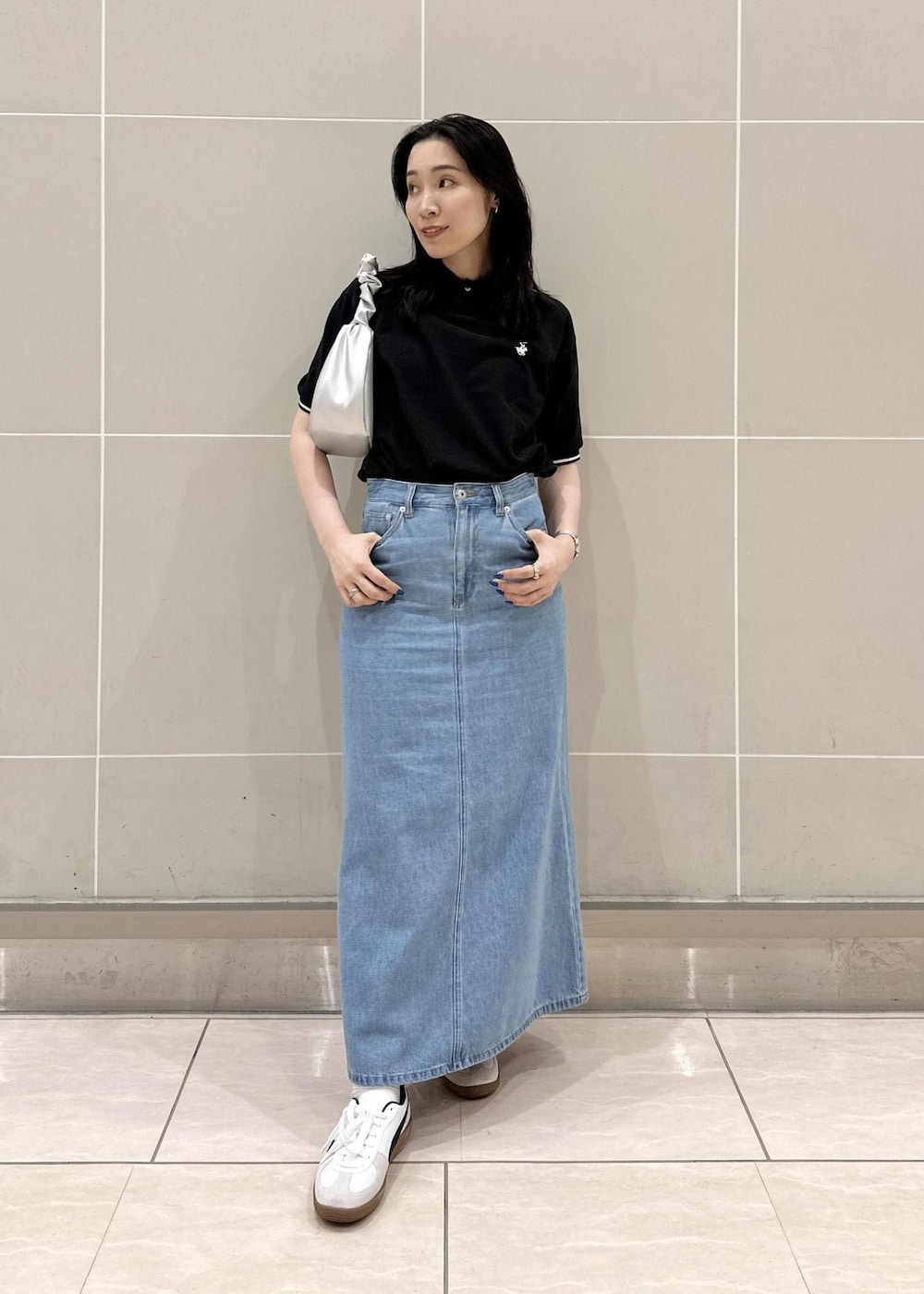 ブルー系のデニムスカート、シルバー系のハンドバッグ、ブラック系のポロシャツを着用したレディースの夏コーディネートの2枚目の写真