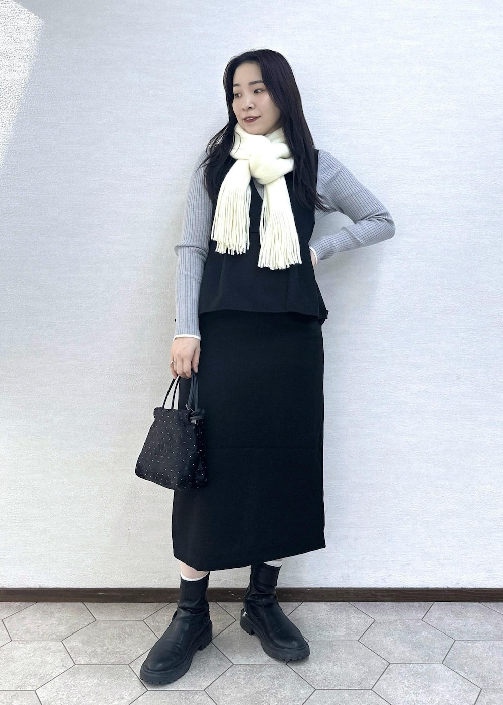 グレー系のニット/セーター、ブラック系のハンドバッグ、ブラック系のジャンパースカートを着用したレディースの冬コーディネートの2枚目の写真