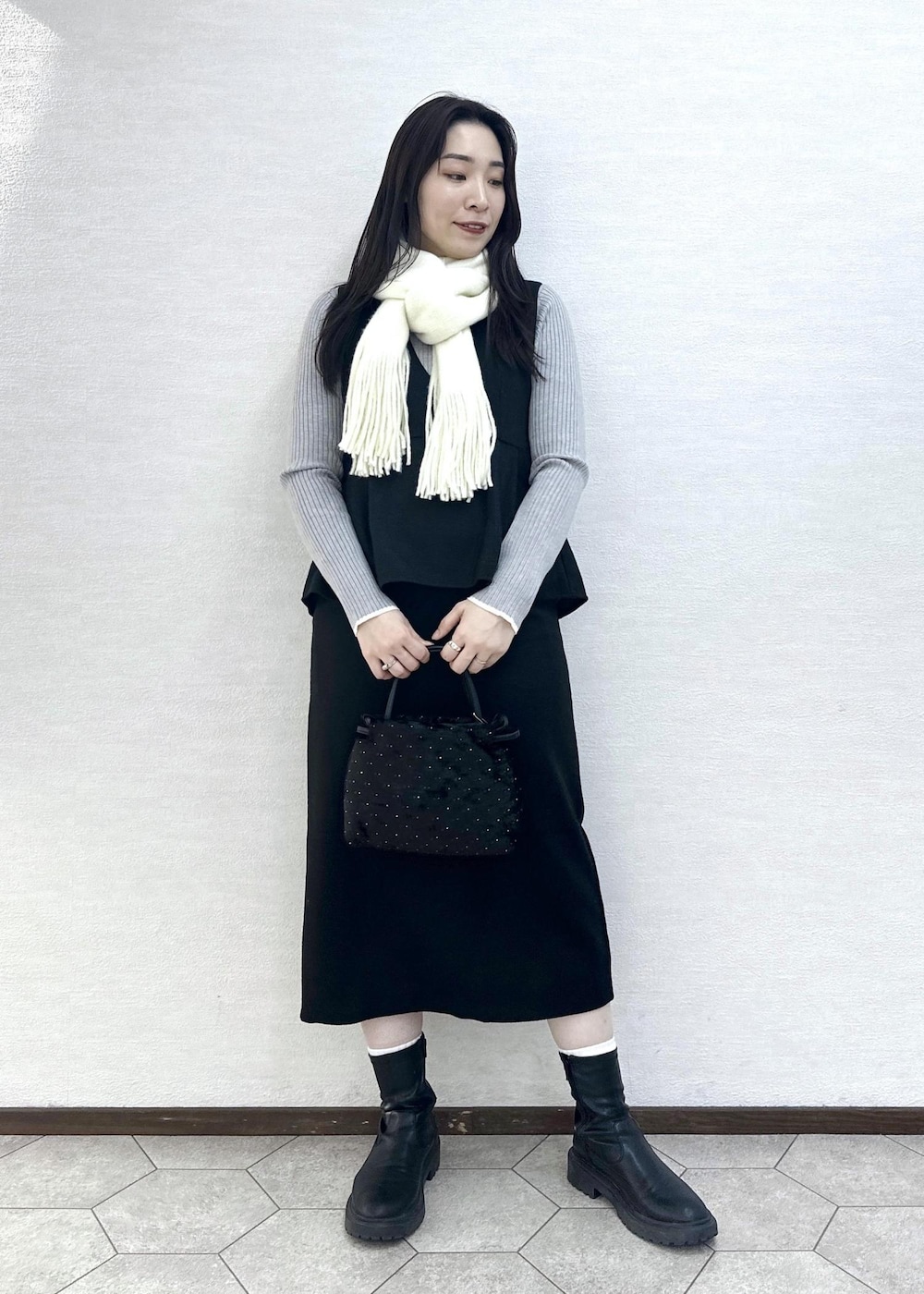 グレー系のニット/セーター、ブラック系のハンドバッグ、ブラック系のジャンパースカートを着用したレディースの冬コーディネートの4枚目の写真