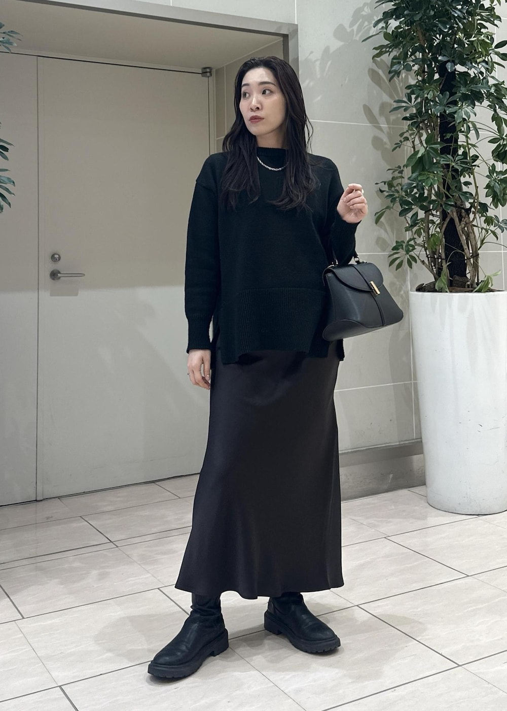 ブラック系のニット/セーター、ブラック系のショルダーバッグ、ブラウン系のスカートを着用したレディースの冬コーディネートの2枚目の写真