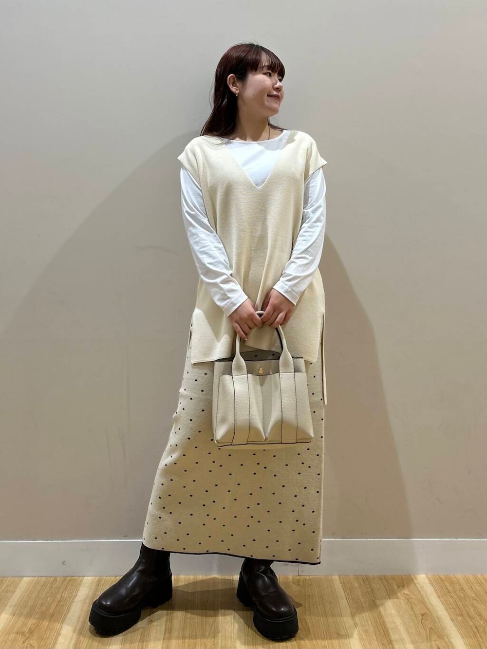 ブラウン系のハンドバッグ、ブラウン系のノーカラーコート、ホワイト系のスカートを着用したレディースの冬コーディネートの2枚目の写真