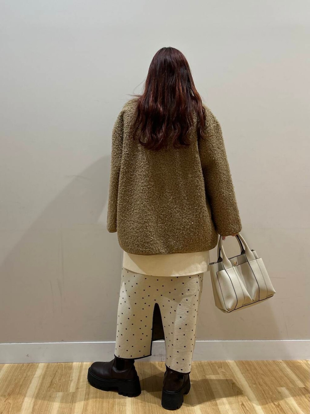 ブラウン系のハンドバッグ、ブラウン系のノーカラーコート、ホワイト系のスカートを着用したレディースの冬コーディネートの4枚目の写真